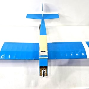 May include: A radio-controlled model airplane featuring a blue and white color scheme. The aircraft has a cream-colored fuselage section, a single main wing with white stripes, and a tail assembly with a blue and white horizontal stabilizer.