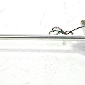 Può includere: Un braccio per giradischi in metallo color argento con testina nera a righe bianche, un contrappeso circolare nero e argento e sottili cavi elettrici a vista che si estendono dal punto di rotazione del meccanismo.