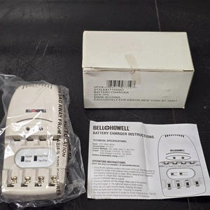 May include: A Bell + Howell battery charger, packaged in plastic, with a white box and instruction manual. The charger has slots for batteries and a switch for quick or slow charging. The box has a label with product information.