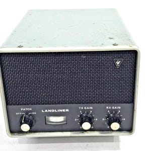 Peut inclure: Un appareil de communication radio Landliner vintage avec un boîtier en métal gris clair et un panneau avant gris foncé. Il comprend une grille de haut-parleur noire, trois boutons de commande noirs étiquetés Patch, TX Gain et RX Gain.