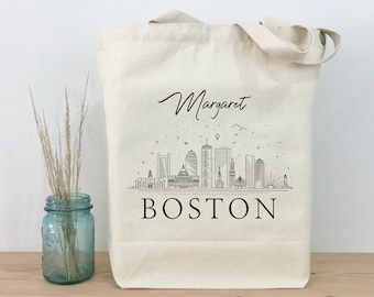 Könnte beinhalten: Eine weiße Canvas-Tragetasche mit schwarzem Text und einer Schwarzweiß-Illustration der Skyline von Boston. Der Text auf der Tasche lautet "Margaret BOSTON".