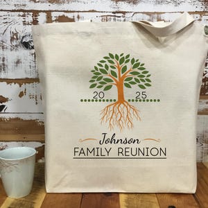 May include: A white canvas tote bag with a green tree design and the text "Johnson FAMILY REUNION". The tree has orange roots and a line of green dots with the numbers 20 and 25.
