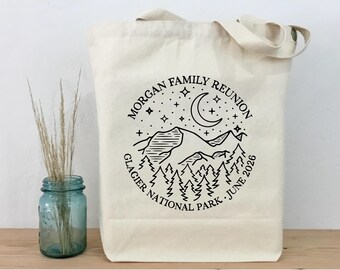 Könnte beinhalten: Cremefarbene Tragetasche mit schwarzem Grafikdesign. Das Design zeigt eine Bergkette, Bäume, Sterne und einen Halbmond mit dem Text "MORGAN FAMILY REUNION" und "GLACIER NATIONAL PARK JUNE 2026".