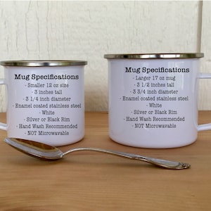 May include: Two white enamel mugs with silver rims, one smaller (7.6 cm tall, 8.3 cm diameter) and one larger (8.9 cm tall, 9.5 cm diameter). Text on the mugs details specifications. A silver spoon rests in front.