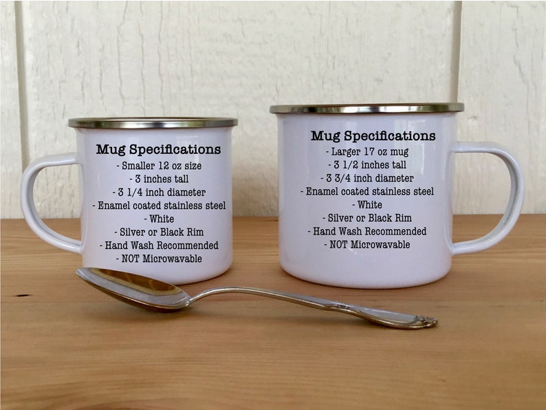 May include: Two white enamel mugs with silver rims, one smaller (7.6 cm tall, 8.3 cm diameter) and one larger (8.9 cm tall, 9.5 cm diameter). Text on the mugs details specifications. A silver spoon rests in front.