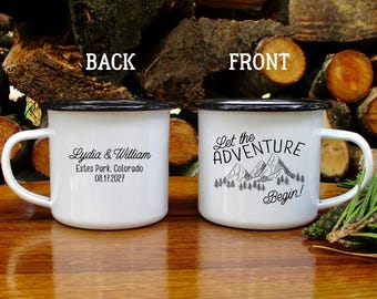 May include: Two white enamel mugs with black rims and handles. One mug reads "Lydia & William, Estes Park, Colorado, 08.17.2027." The other mug says "Let the ADVENTURE Begin!" with a mountain graphic.