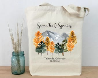 Könnte beinhalten: Beige Tragetasche mit einem Aquarelldesign von Bergen und Bäumen in Orange- und Grüntönen. Die Namen "Samantha & Spencer" und der Ort "Telluride, Colorado 10.15.2026" sind auf der Tasche aufgedruckt.