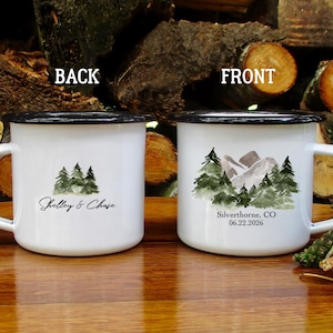 May include: Two white enamel mugs with black rims and handles. One mug features a watercolor design of trees and the text "Shelley & Chase." The other mug has a mountain and tree design with the text "Silverthorne, CO 06.22.2026."