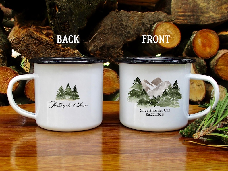May include: Two white enamel mugs with black rims and handles. One mug features a watercolor design of trees and the text "Shelley & Chase." The other mug has a mountain and tree design with the text "Silverthorne, CO 06.22.2026."