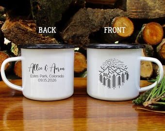 Könnte beinhalten: Zwei weiße Emaille-Tassen mit schwarzen Rändern und Griffen. Eine Tasse zeigt die Namen "Allie & Aaron", Ort und Datum. Die andere Tasse hat ein Berg- und Wald-Design mit einer Sonne.