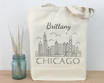 Könnte beinhalten: Eine weiße Canvas-Tragetasche mit schwarzem Text und einer schwarzen Strichzeichnung der Skyline von Chicago. Der Text auf der Tasche lautet "Brittany CHICAGO".