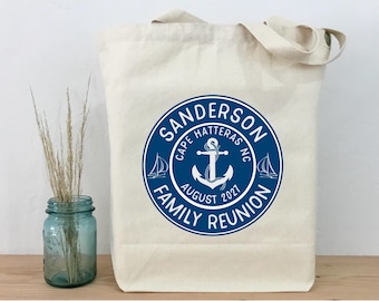 Könnte beinhalten: Eine cremefarbene Canvas-Tragetasche mit einer kreisförmigen blauen Grafik, die einen Anker, zwei Segelboote und den Text SANDERSON FAMILY REUNION, CAPE HATTERAS NC, AUGUST 2021 zeigt. Die Tasche hat zwei Tragegriffe und eine rechteckige Form.