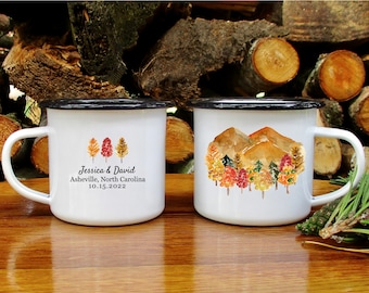May include: Two white enamel mugs with black rims. One mug features a watercolor illustration of fall trees and mountains. The other mug has a watercolor illustration of three trees and the text "Jessica & David, Asheville, North Carolina, 10.15.2022".