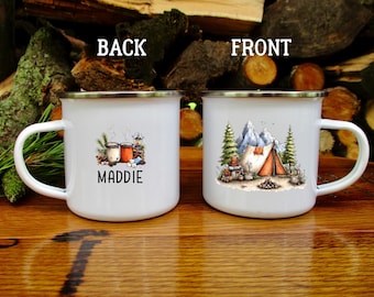 May include: Two white enamel mugs with silver rims. The left mug features a graphic of two mugs, a lantern, and the name MADDIE. The right mug displays a camping scene with a tent, pine trees, and mountains. The text BACK and FRONT is visible.