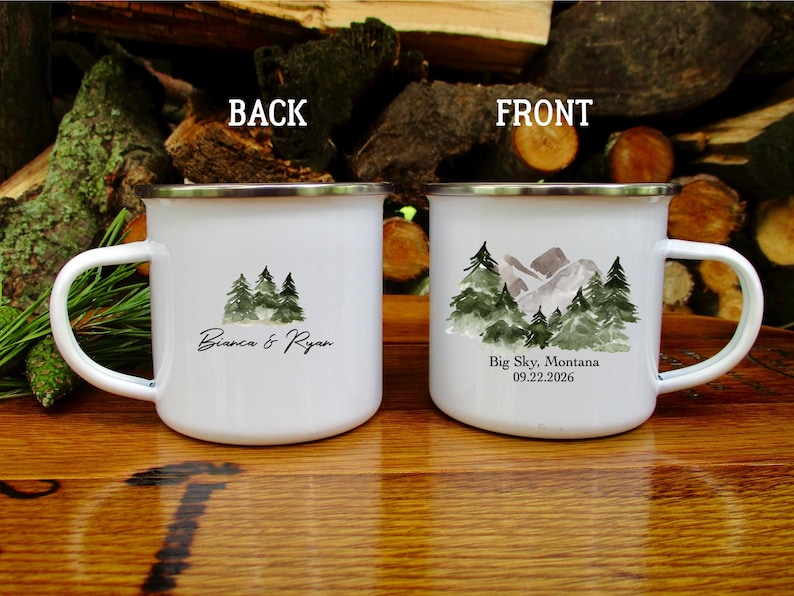 May include: White enamel mug with a silver rim, featuring a watercolour design of pine trees and mountains. The front of the mug reads "Big Sky, Montana 09.22.2026". The back of the mug has a watercolour design of pine trees and the names "Bianca & Ryan".