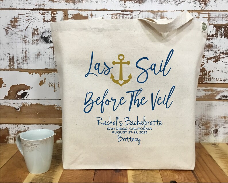 May include: A white canvas tote bag with a blue and gold design. The text on the bag reads "Last Sail Before The Veil" with an anchor symbol. The text below reads "Rachel's Bachelorette, San Diego, California, August 27-29, 2023, Brittney".