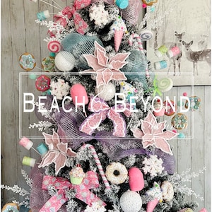 May include: A pink and blue Christmas tree decorated with candy canes, donuts, cupcakes, and other sweet treats. The tree is topped with a large pink lollipop. The tree is decorated with the text "Beach & Beyond".
