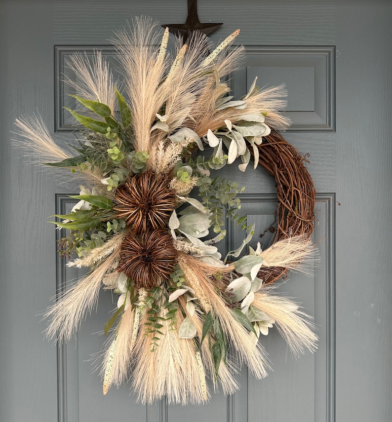 May include: A brown twig wreath decorated with dried beige and white pampas grass, dried eucalyptus, and brown dried flower heads.