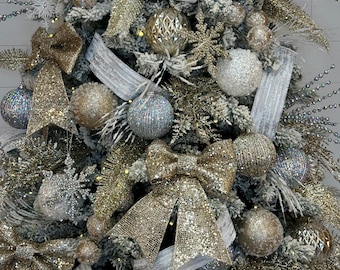 May include: A flocked Christmas tree decorated with gold and silver ornaments, bows, and ribbon. The tree is adorned with a variety of textures, including glitter, sequins, and beads.