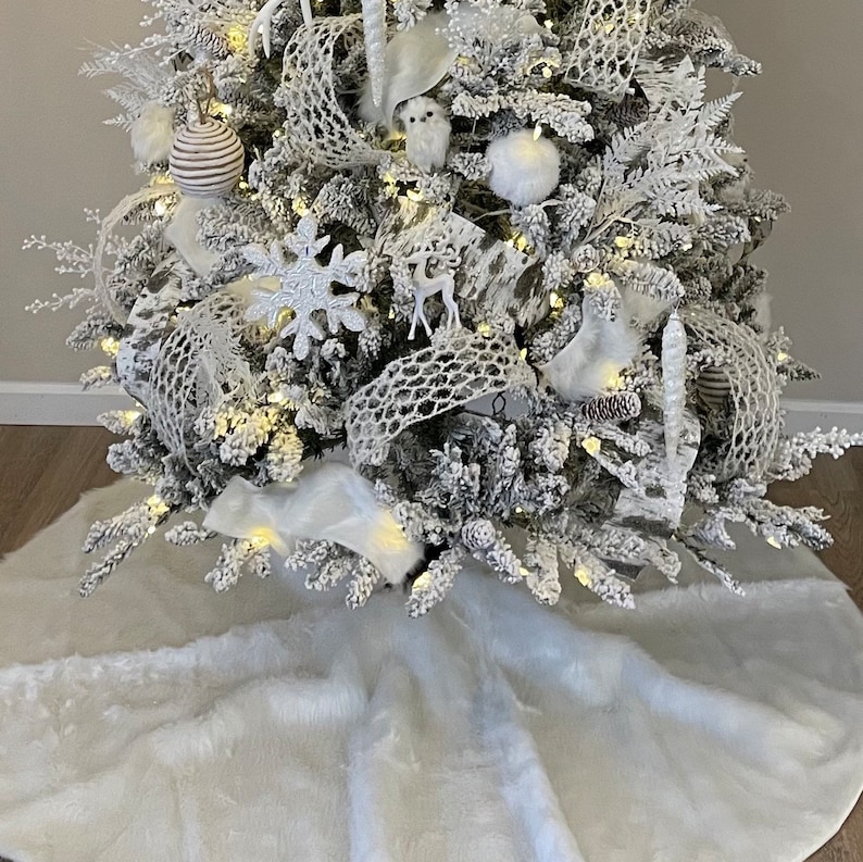 May include: A white faux fur Christmas tree skirt with a white flocked Christmas tree decorated with white and silver ornaments, lights, and ribbon.