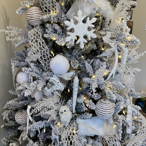 May include: A snowy white Christmas tree decorated with white and brown ornaments, white faux fur, birch bark ribbon, and white snowflake ornaments.