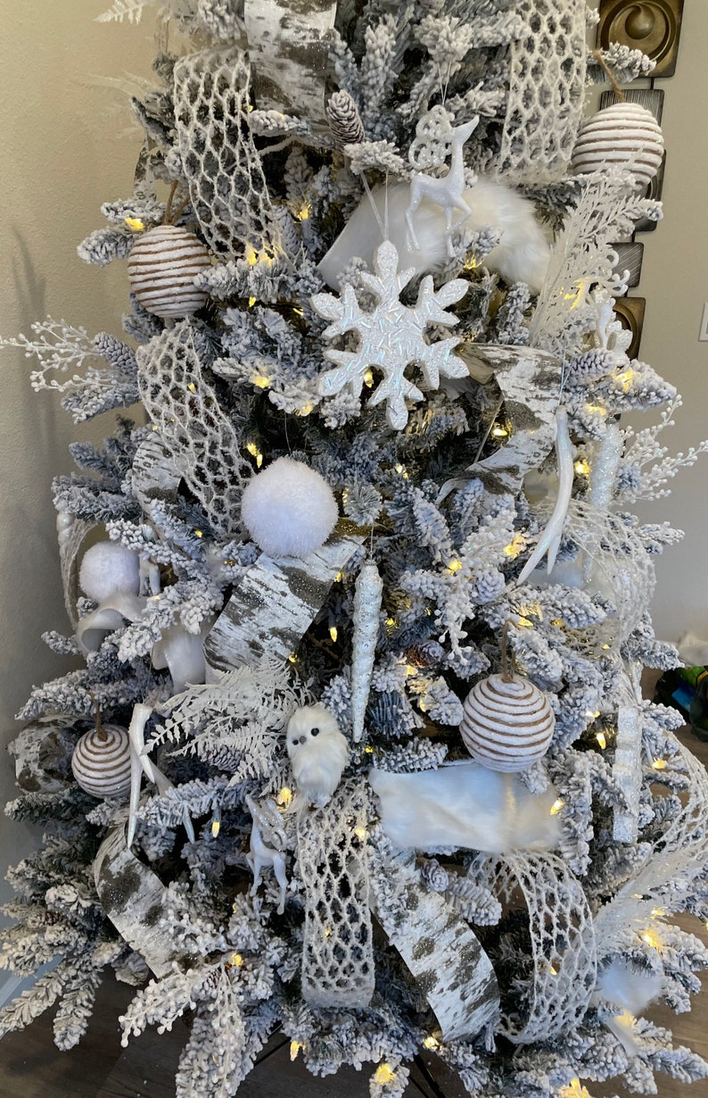 May include: A snowy white Christmas tree decorated with white and brown ornaments, white faux fur, birch bark ribbon, and white snowflake ornaments.