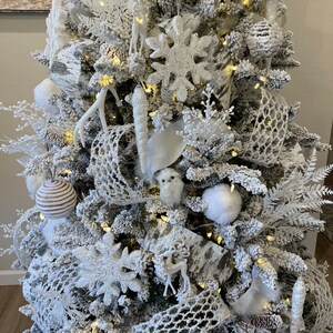 May include: A white flocked Christmas tree decorated with white and brown ornaments, white owls, white deer, white antlers, and white snowflake ornaments.