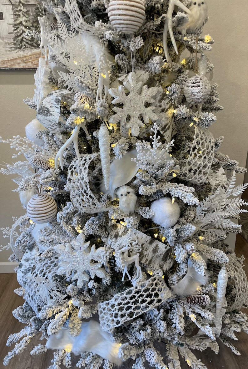 May include: A white flocked Christmas tree decorated with white and brown ornaments, white owls, white deer, white antlers, and white snowflake ornaments.
