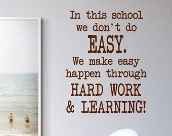 May include: A motivational quote on a white wall with a framed picture of a beach scene. The quote reads: "In this school we don't do EASY. We make easy happen through HARD WORK & LEARNING!"