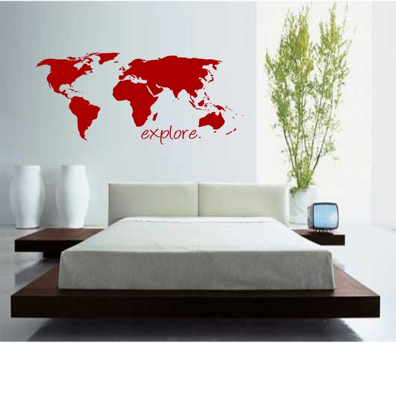 K&ouml;nnte beinhalten: Ein roter Wandaufkleber mit einer Weltkarte und dem Wort "explore" darunter. Der Aufkleber befindet sich an einer wei&szlig;en Wand &uuml;ber einem braunen Plattformbett mit wei&szlig;er Bettw&auml;sche.