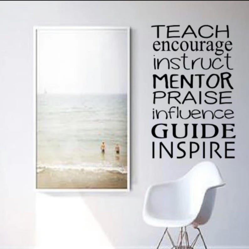 May include: A black and white photo of a beach scene is framed and hanging on a white wall.  The wall also has a black vinyl decal with the words "Teach, Encourage, Instruct, Mentor, Praise, Influence, Guide, Inspire".
