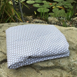 Puede incluir: Tela doblada con un patrón de lunares blancos sobre fondo gris. La tela descansa sobre una gran roca texturizada, con un estanque y vegetación en el fondo.