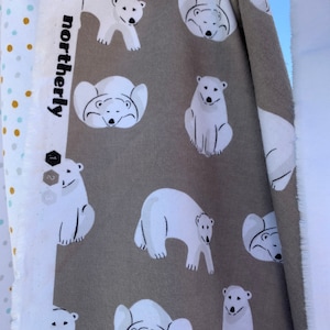 Puede incluir: Una tela gris con un estampado de osos polares blancos. Los osos están en varias poses, incluyendo de pie, sentados y acostados. La tela tiene la palabra "northerly" impresa.