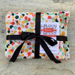 May include: A white fabric with a colorful polka dot pattern is wrapped in black ribbon and tied with a bow. The fabric is labeled "Sewn" with a small tag that says "Handmade for you by MH".