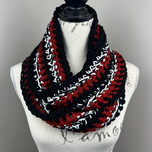 May include: A black, white, and burgundy crocheted infinity scarf. The scarf is made with a chunky yarn and has a textured pattern.
