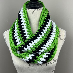 May include: A green, black, and white crocheted infinity scarf. The scarf is displayed on a white mannequin.