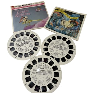 May include: Vintage View-Master set featuring "The World of Liddle Kiddles." The set includes three white viewer reels and two illustrated boxes. The boxes display the title and cartoon images. The reels have small text and numbered frames.