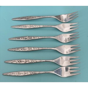 May include: Six silver forks with a textured handle design. The forks have three tines and are arranged on a light blue background. The handles have a repeating geometric pattern.