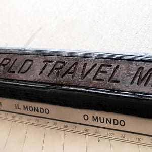 May include: A close-up of a wooden sign with the text "IN FAMILY WORLD TRAVEL MAP" in raised letters. The sign is dark brown and has a worn, rustic look.
