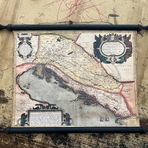 Può includere: Un'antica mappa di una regione, forse l'Europa, con caratteristiche geografiche dettagliate e testo. La mappa è stampata su carta invecchiata e montata su barre a scorrimento in legno nero con terminali decorativi.