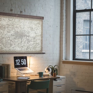 May include: A home office workspace with a vintage map hanging on the wall, a laptop computer on a desk, a lamp, a globe, and a typewriter.