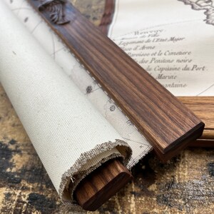 May include: A rolled up canvas map with a wooden dowel and carved wooden finial. The map is printed with text in French, including the words "Logement de Wast Majer", "Ince & Arme", "Parvisse et le Cimetiere", "des Penitens noirs", "he Capuaine du Port", "Marine", and "nhune".