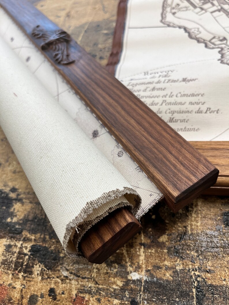 May include: A rolled up canvas map with a wooden dowel and carved wooden finial. The map is printed with text in French, including the words "Logement de Wast Majer", "Ince & Arme", "Parvisse et le Cimetiere", "des Penitens noirs", "he Capuaine du Port", "Marine", and "nhune".