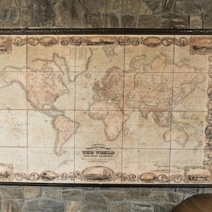 May include: A detailed, vintage world map, mounted on a wall. The map, with a sepia colour scheme, is framed by an elaborate border. The map is divided into rectangular tiles and includes the text "THE WORLD".