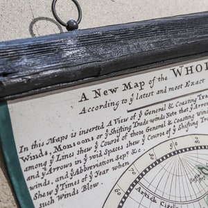 May include: A vintage map of the world with a black wooden frame and a metal hanging ring. The map is titled "A New Map of the Whole" and includes text about the general and coasting trade winds.