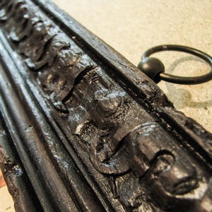 Detailed close-up of an ornate carved wooden scroll hanger with decorative black finish and metal hanging ring. Handcrafted vintage map frame designed for antique world map canvas wall art.