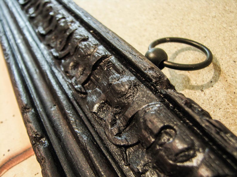 Detailed close-up of an ornate carved wooden scroll hanger with decorative black finish and metal hanging ring. Handcrafted vintage map frame designed for antique world map canvas wall art.