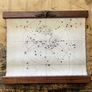May include: A vintage-style map of a constellation, framed in a dark wood frame with a decorative carved wooden top. The map shows a constellation of stars in the shape of a dragon.