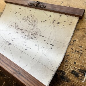 May include: A vintage-style map print with a celestial design, framed in a dark wood frame with a decorative top.