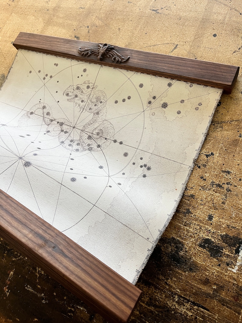 May include: A vintage-style map print with a celestial design, framed in a dark wood frame with a decorative top.